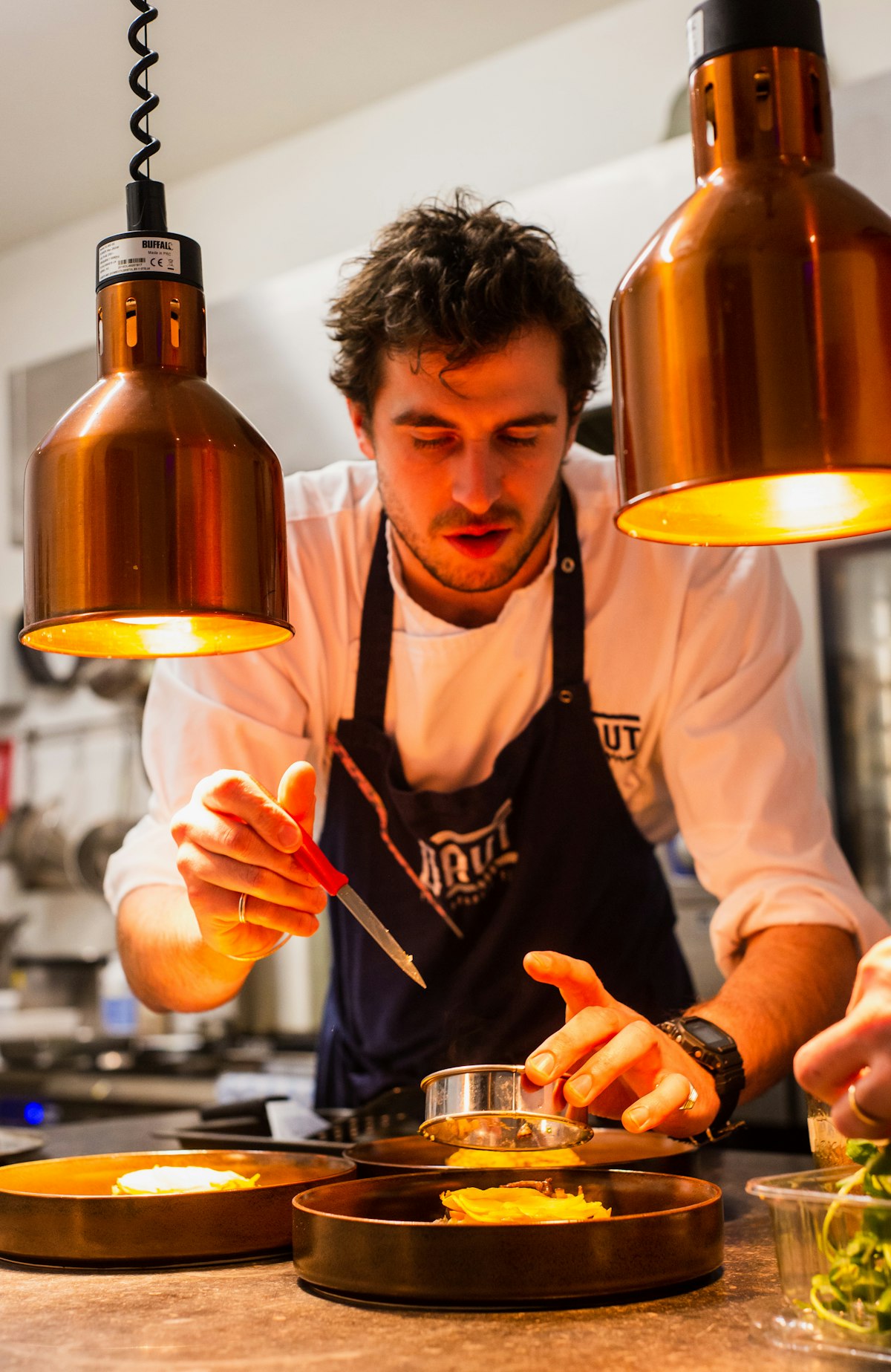 Chef dressant un plat sous des lampes chauffantes